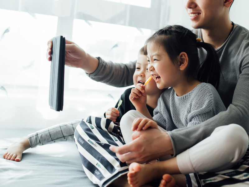 A father, son and daughter are animatedly participating in a video call while sitting in a brightly-lit room